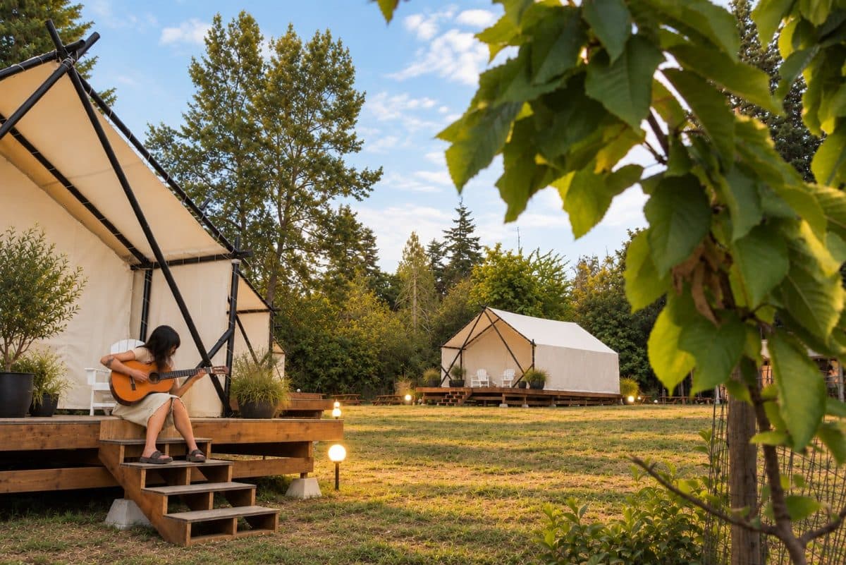 A camper plays guitar on the steps of a canvas tent among the trees