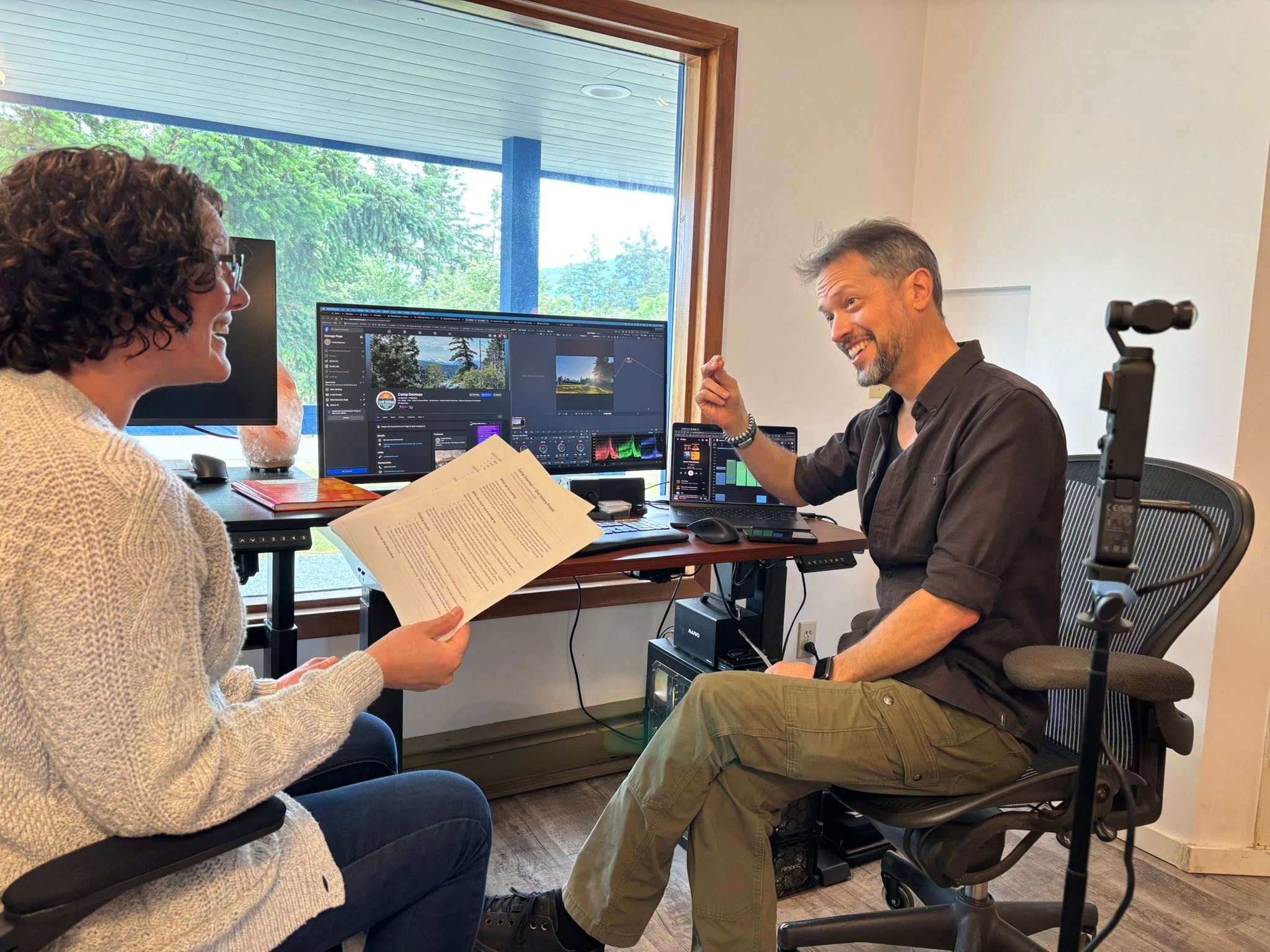 Two Camp Denman collaborators working together at an edit-suite desk overlooking the trees