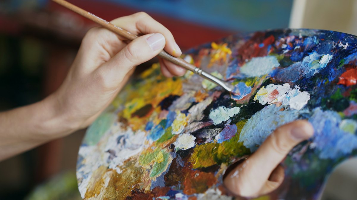 Close-up of hands mixing paint on a palette